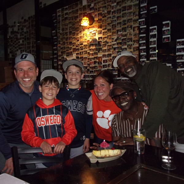A group of six people smiling at a hibachi table with cheesecake and drinks.