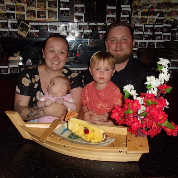 A family of four, including a baby, smiles at Shogun Japanese Steakhouse with a pineapple boat.