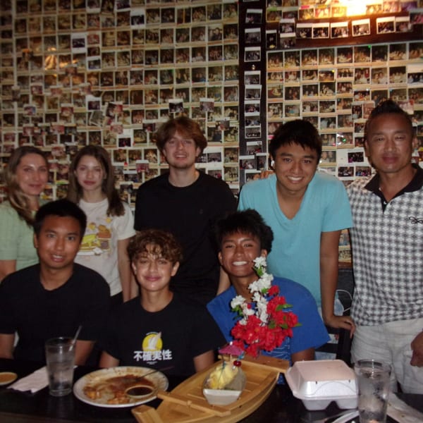 A group of eight people smiling at a table in Shogun Japanese Steakhouse, with a wall of photos behind them.
