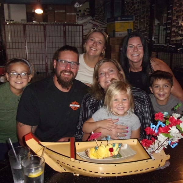 A family of seven smiles at Shogun Japanese Steakhouse, with a pineapple dessert boat in the foreground.