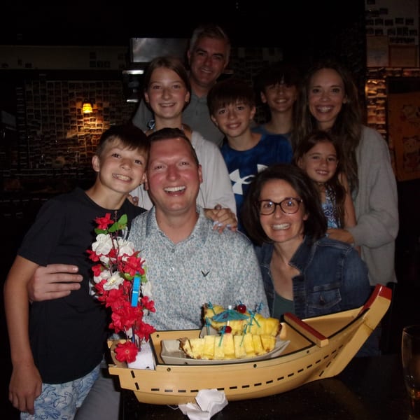 A large family group smiling at Shogun Japanese Steakhouse, with a pineapple dessert boat in the foreground.