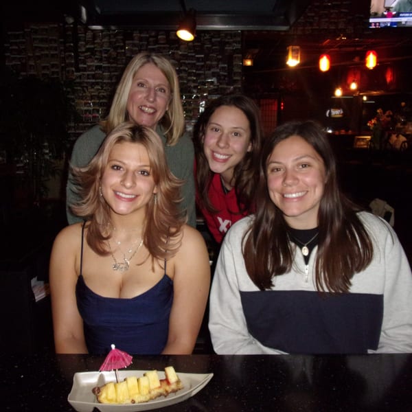 Four smiling women pose at a hibachi restaurant table with a pineapple dessert in the foreground.