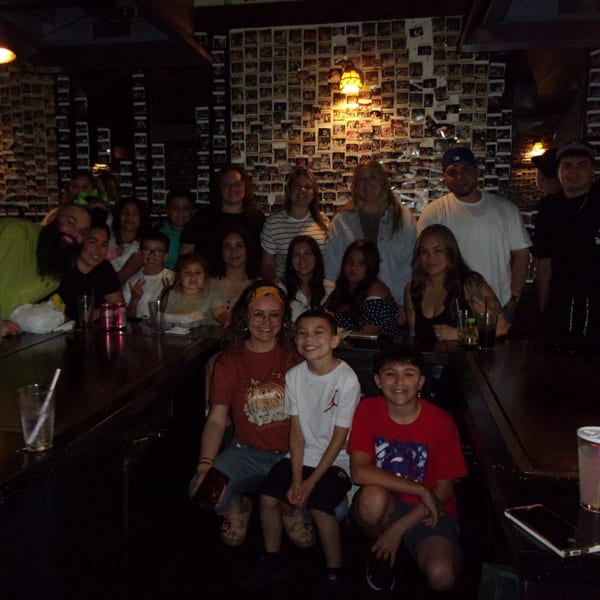A large group of adults and children smiling at the camera in a dimly lit Shogun Japanese Steakhouse.