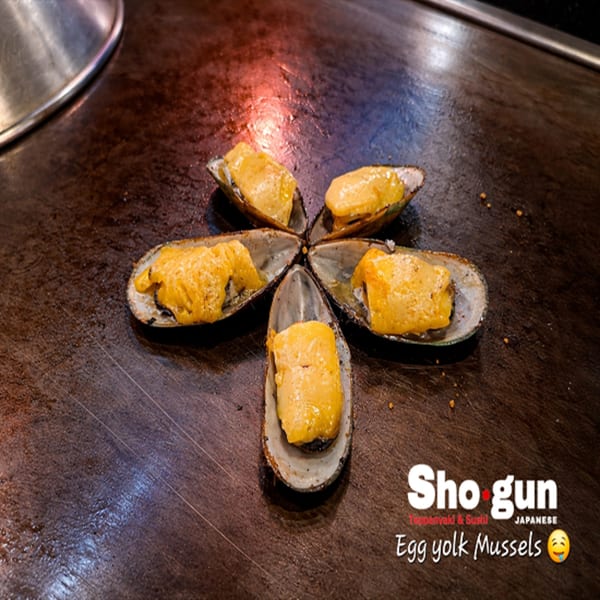 Five egg yolk mussels arranged in a star shape on a dark teppanyaki grill.