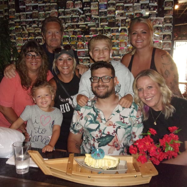 A family of eight, including children, smiles at a Shogun Japanese Steakhouse hibachi table with dessert.