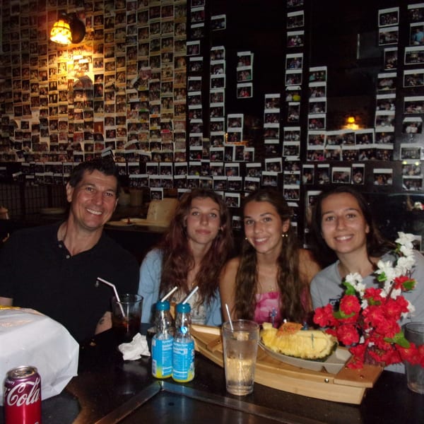 A family of four smiles at a hibachi table in Shogun Japanese Steakhouse, with drinks and a pineapple dessert.