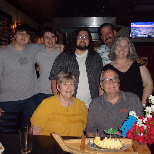 Seven people smiling for a group photo at a Shogun Japanese Steakhouse hibachi table.