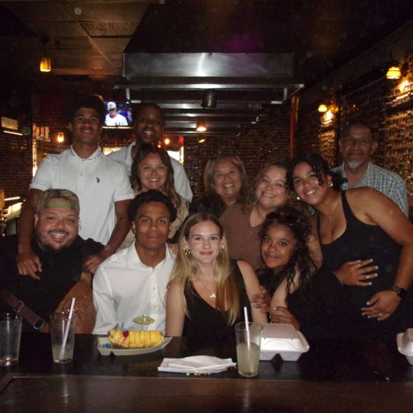 A large group of smiling people gathered around a hibachi grill at Shogun Japanese Steakhouse.