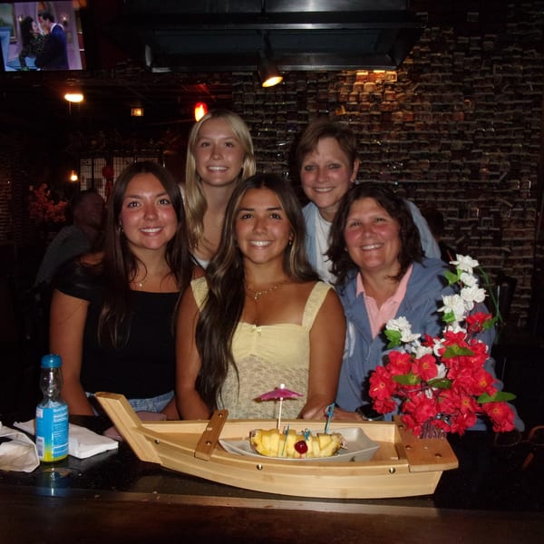 Five women smiling at a hibachi restaurant, with a pineapple dessert boat in the foreground.